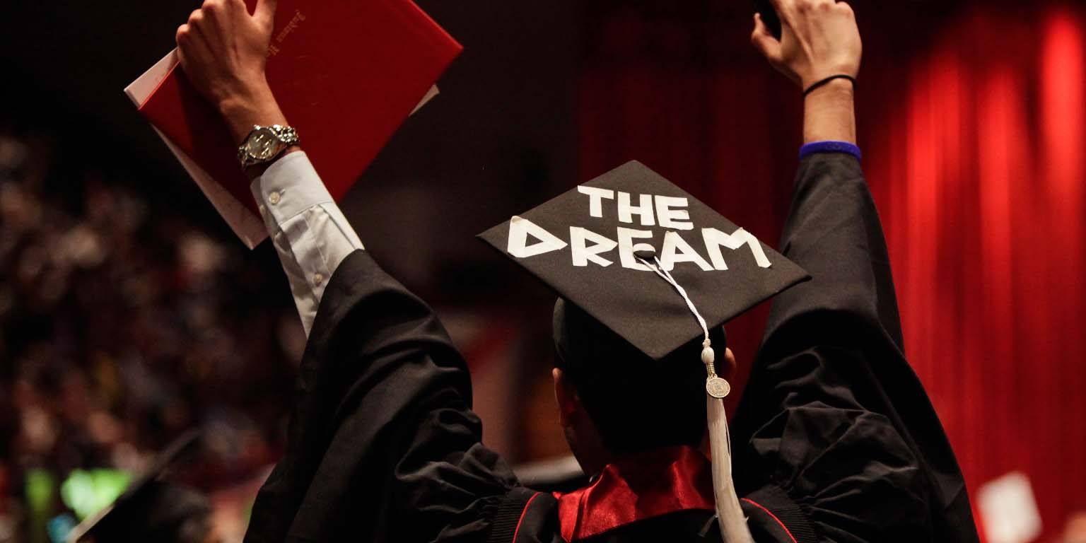 A back view of graduate with "THE DREAM" written on their mortarboard.